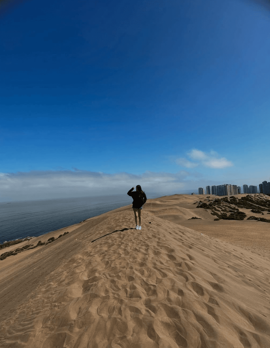 Viajera en la cima de las dunas de Concón con el mar y los edificios de Reñaca al fondo